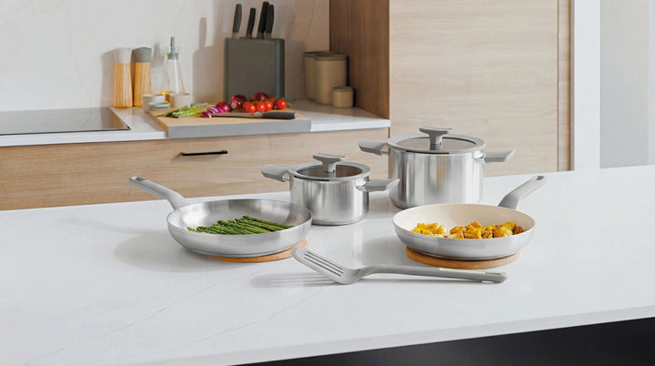 28 cm frying pan with a silver finish on a white countertop, alongside pots and asparagus.